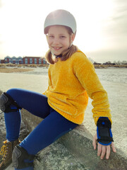 Portrait of pretty teenager girl in yellow pullover, helmet and inline protective equipment posing...