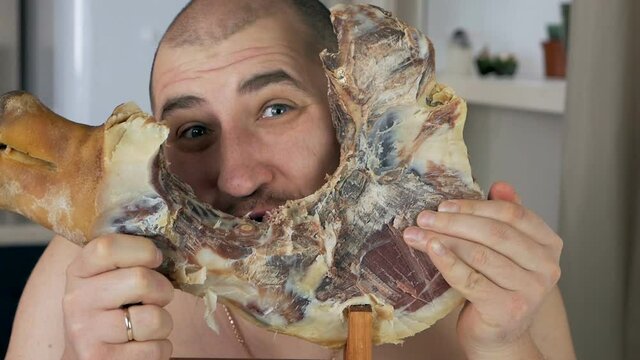 The bald man is disgusting, gnawing Spanish serrano ham on the bone in his apartment
