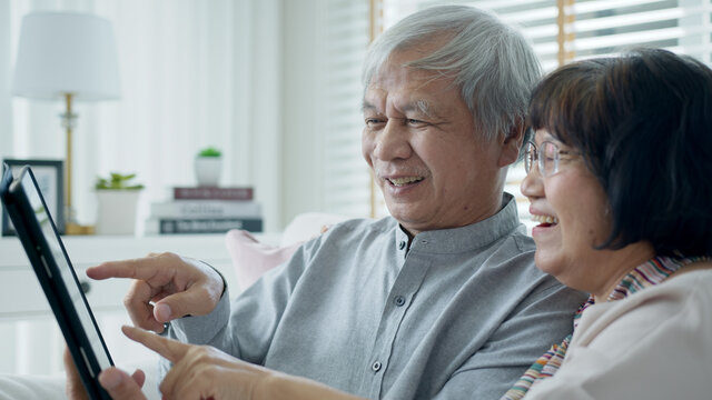 Candid old asian retired couple use tablet computer to transfer money online or financial payment and read text, smile or laugh with happy and positive. Senior asia with digital technology concept.