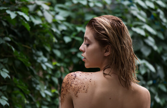 Beautiful young woman uses coffee scrub and peeling on her body front of plant tropical green leaves background.