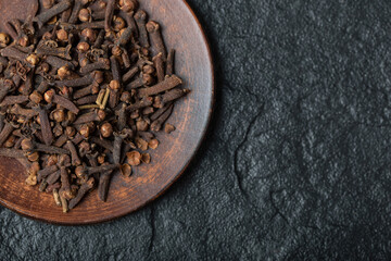 A brown plate full of dried cloves on a dark background