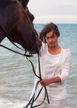 Joven amazona con vestido blanco domando a su caballo marron sin montura en la playa