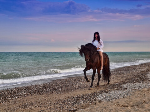 Joven amazona con vestido blanco domando a su caballo marron sin montura en la playa