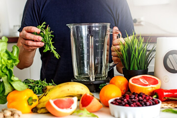 A man prepares a wellness food smoothie with fresh herbs, bananas and fresh berries in a blender 