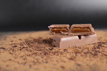 A cut of chocolate stuffed with caramel chocolate bar lies on the cocoa on a black background with place for text and a copy of the day of chocolate
