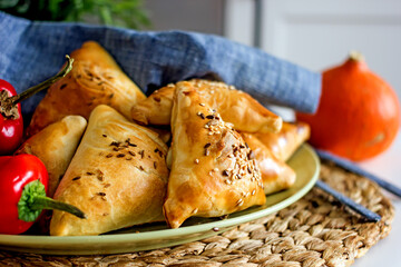 Samsa oriental Uzbek puff pastry pies with meat and pumpkin on a plate on the table, close-up. Triangular pies with sesame seeds, national authentic pastries