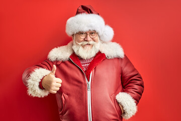 caucasian santa man express positive emotions, showing thumbs up, wearing red coat and hat, smile. isolated red background