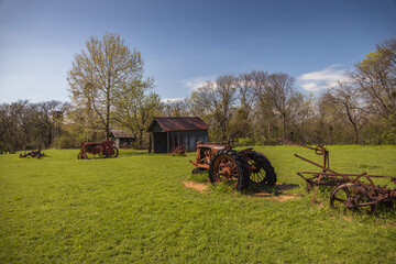 Old rusty farm equipment and tractor by a barn
