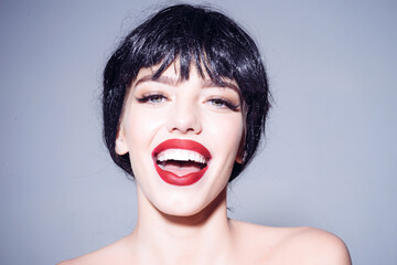 Girl on happy smiling face. Lady in black wig with make up on grey background closeup. Beautiful smile concept. Woman with attractive red lips and white teeth.