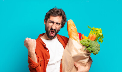 young bearded man shouting aggressively with an angry expression or with fists clenched celebrating...
