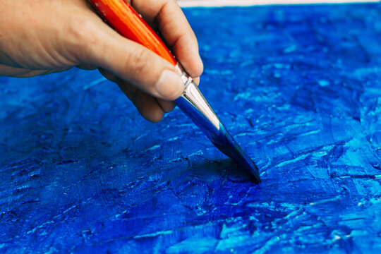Selective focus of a hand with an artist brush painting a blue picture