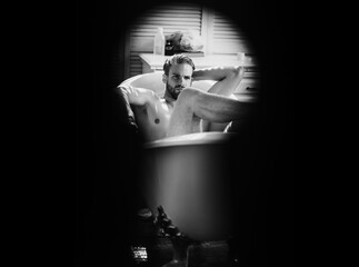 Sexy man relax in bath seen in keyhole, secret. Privacy. The concept of voyeurism, curiosity,...