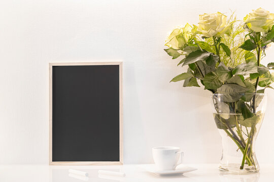 Modèle de tableau noir en ardoise avec espace vide pour logos, inscription publicitaire. Cadre en mode portrait sur un espace de travail avec des roses et des craies.
