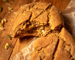 Closeup broken homemade fresh bread and pumpkin seeds on parchment paper wooden table