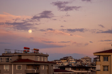 Moon between the clouds and the buildings with the sunset view