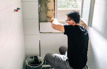 Male bricklayer laying tile on the wall with spatula