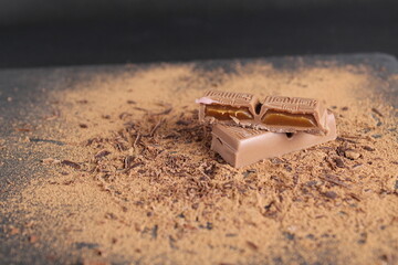 A cut of chocolate stuffed with caramel chocolate bar lies on the cocoa on a black background with place for text and a copy of the day of chocolate