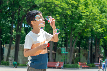 Young boy blowing bubbles in the park in the brigth summer day in park