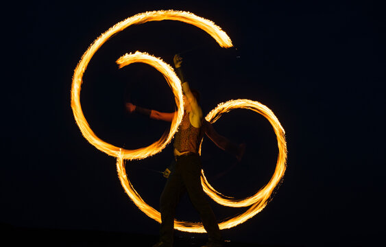 Fire poi artist perform burning reels with glowing, tails in motion on dark sky outdoors, stunt