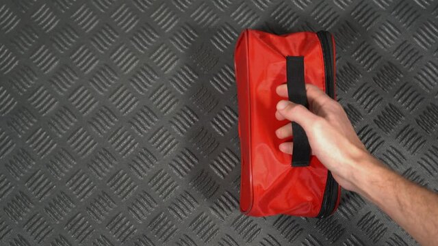 Closeup top view flatlay 4k stock video footage of male hand taking red case of first aid medical kit laying on black plastic rubber mat in boot of automobile