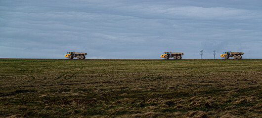 Fototapeta na wymiar three yellow Volvo A40E articulated dump truck articulated earth movers in a convoy kicking up dust as they navigate across Salisbury Plain, Wiltshire UK