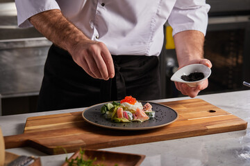 young chef adds a little spices and dressings to make dish taste amazing in order to serve clients of restaurant with such yummy meal