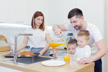 Obraz na płótnie Canvas Young happy family with two young sons preparing breakfast together in their kitchen
