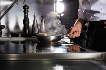 Chef cooking in frying pan on kitchen stove, cropped unrecognizable cook preparing food. steam comes from pan