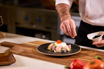 young chef adds a little spices and dressings to make dish taste amazing in order to serve clients of restaurant with such yummy meal