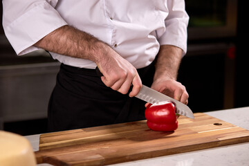 close up of male hand cutting pepper on cutting board in restaurant kitchen. cooking, food and restaurant concept