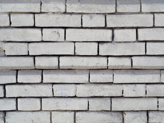 White brick background (pattern) of rough, uneven, carelessly painted over with paint or plaster. The textured surface of the old exterior walls of an industrial building. Chips, cracks and protrusion