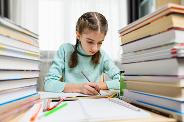 Schoolgirl doing homework at her desk. Next to the girl are tall stacks of books and textbooks.
