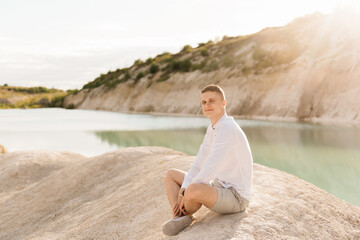 Fototapeta na wymiar Beautiful young guy travels the world near a blue lake and sand at sunset