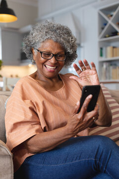 African american senior woman smiling and waving while having a video call on smartphone at home