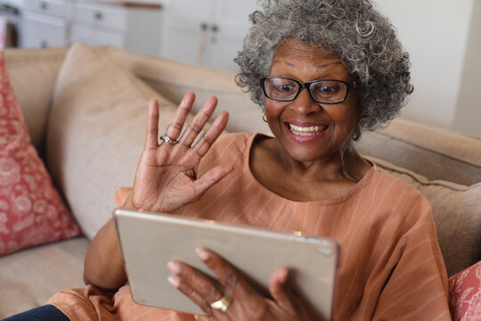 African american senior woman smiling and waving while having a video call on digital tablet at home