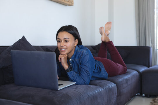 African american woman using laptop lying on the couch at home
