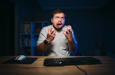 An emotional online worker gets angry while working at night on the computer. Angry programmer...