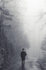 Man walking alone on a road through a dark foggy forest