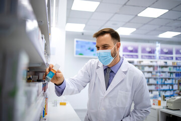 Pharmacist wearing face mask and white coat choosing appropriate vitamins in pharmacy store to sell to the customer during corona virus pandemic. Healthcare and medicine.