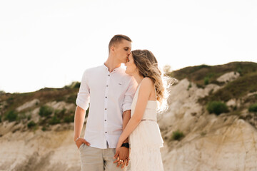 A beautiful young couple in love, a man and a woman embrace, kiss near a blue lake and sand at sunset. Vacation at the sea on the beach, sunset, morning, honeymoon, tropics, ocean, girl, relationship.