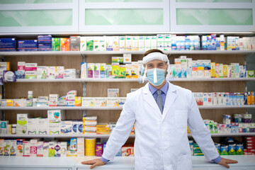 Portrait of pharmacist wearing face shield and white coat standing in pharmacy store during corona virus pandemic.