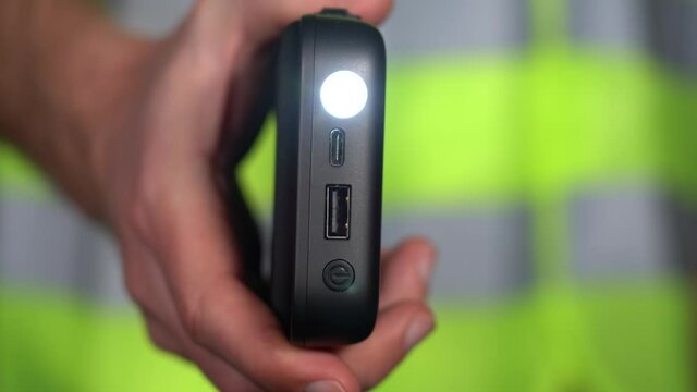Closeup view 4k stock video footage of adult white man dressed in bright yellow reflective vest or safety jacket holds modern electronic device with function of emergency signal flashlight