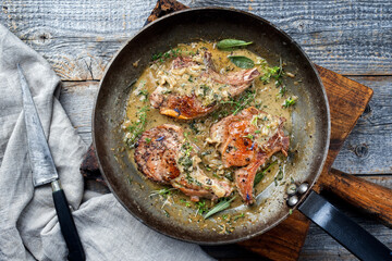 Traditional barbecue dry aged veal chops with herbs in butter jus served as top view in a rustic iron pan on a rustic wooden board