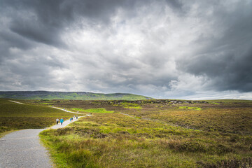 People, tourists walking on gravel path or trail towards Cuilcagh Mountain Park with stormy, dramatic sky in background, Northern Ireland