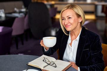 manager woman sitting in restaurant with notebook, drinking cup of coffee, smiling, enjoying free time