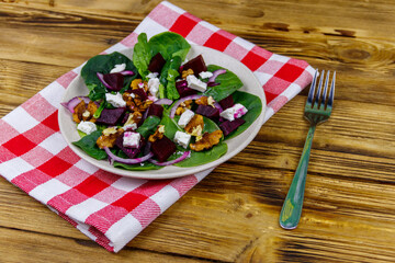 Tasty spinach salad with boiled beetroot, feta cheese, walnut and red onion on wooden table. Healthy vegetarian food