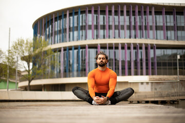 Athlete having a meditation session after intense outdoor training. The young attractive bearded man is relaxing in yoga position