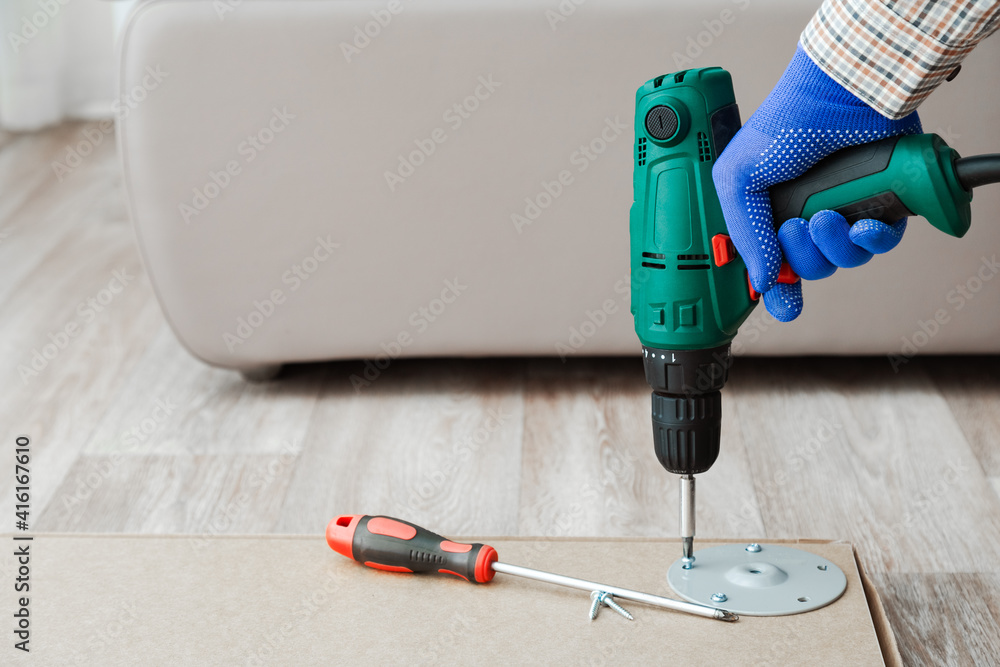 Wall mural electric drill works in handyman hands at home. furniture assembly process, master collects table fu