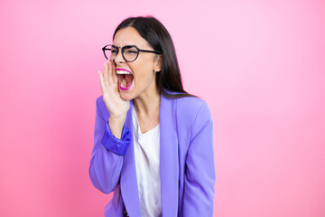 Young business woman wearing purple jacket over pink background shouting and screaming loud to side with hand on mouth