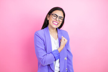 Young business woman wearing purple jacket over pink background feeling happy, positive and successful, motivated when facing a challenge or celebrating good results